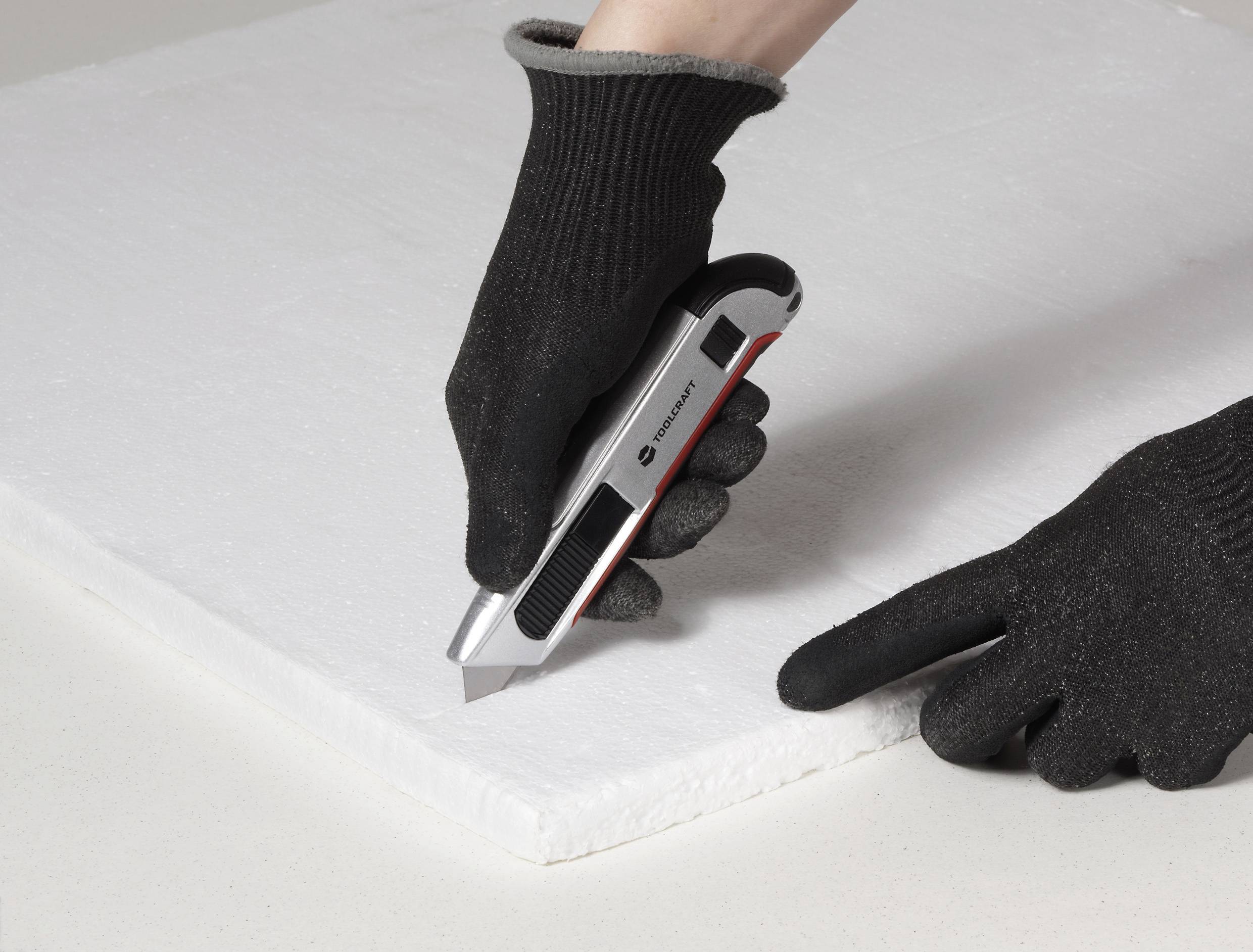 En persons handskklädd hand som använder en multikniv för att skära ett vitt skumstycke på en plan yta, vilket illustrerar ett gör-det-själv-projekt eller hantverksarbete.