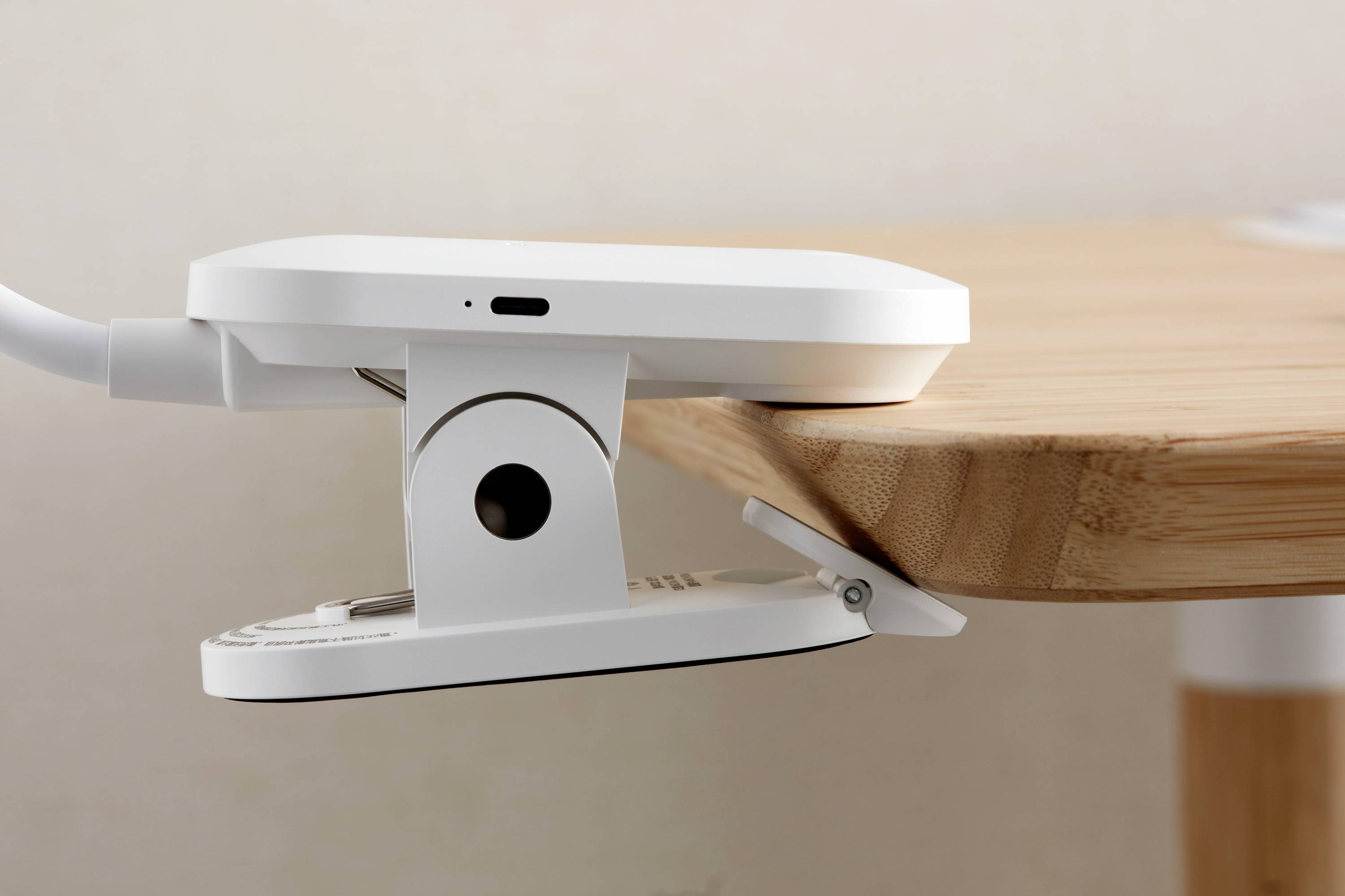 En vit enhet som är fäst vid en träkant. Det verkar vara en teknisk laddare med kabel som är monterad på ett skrivbord.