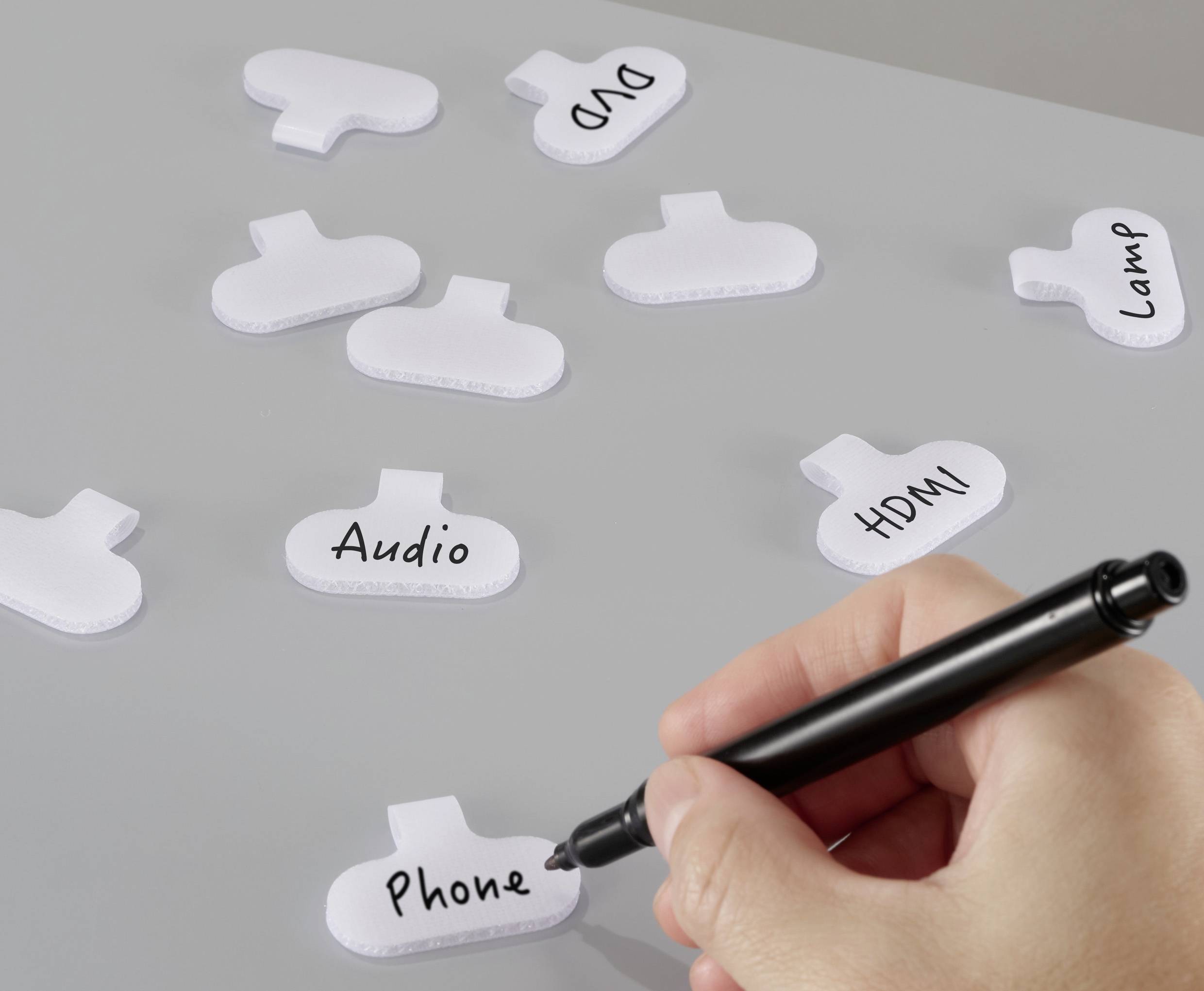 En hand skriver 'Telefon' på en vit kabeletikett; andra etiketter visar 'Ljud', 'HDMI' och 'Lampa', vilket indikerar organisering av kablar.