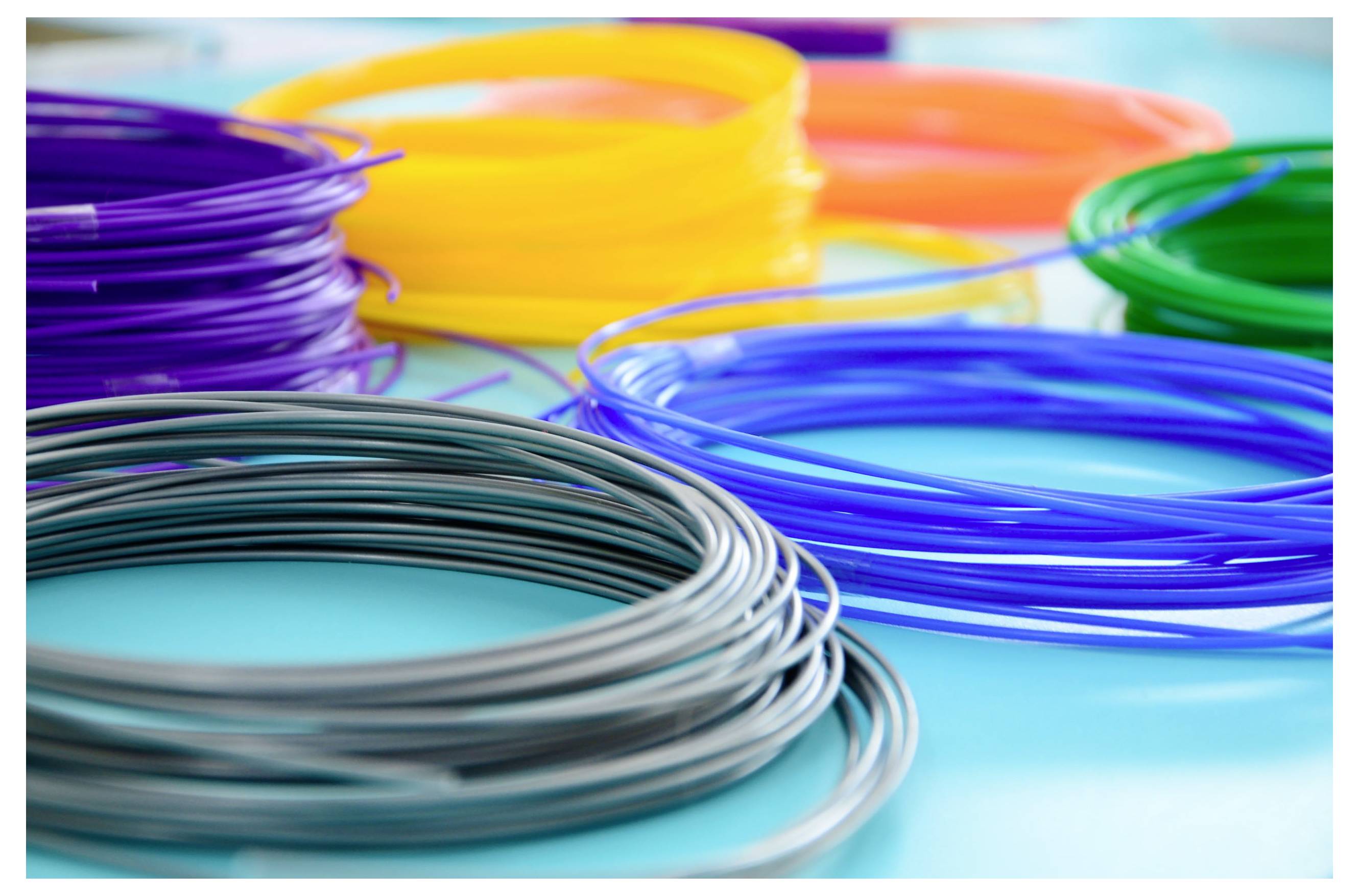 Lindor av färgglatt filament i lila, gult, orange, blått och grått, arrangerade på en ljusblå yta, avsedda för 3D-utskrift.