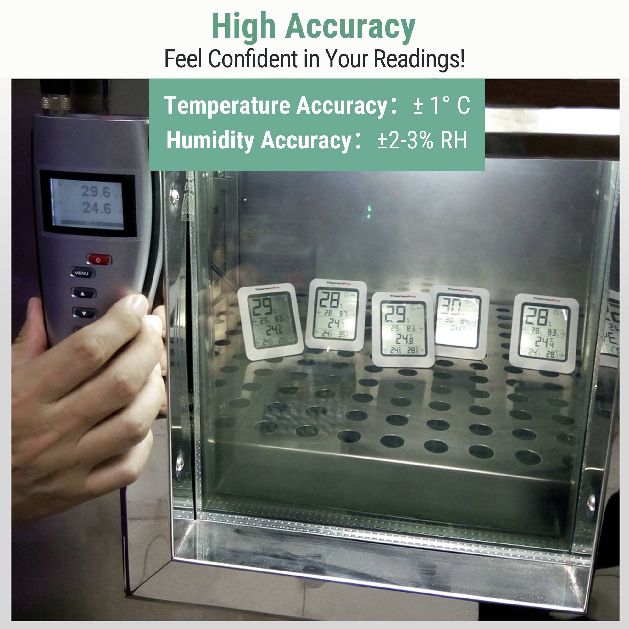 En person använder en termometerenhet på en låda med fyra digitala termometrar som visar liknande temperaturer runt 24-29°C, märkta med hög noggrannhet.