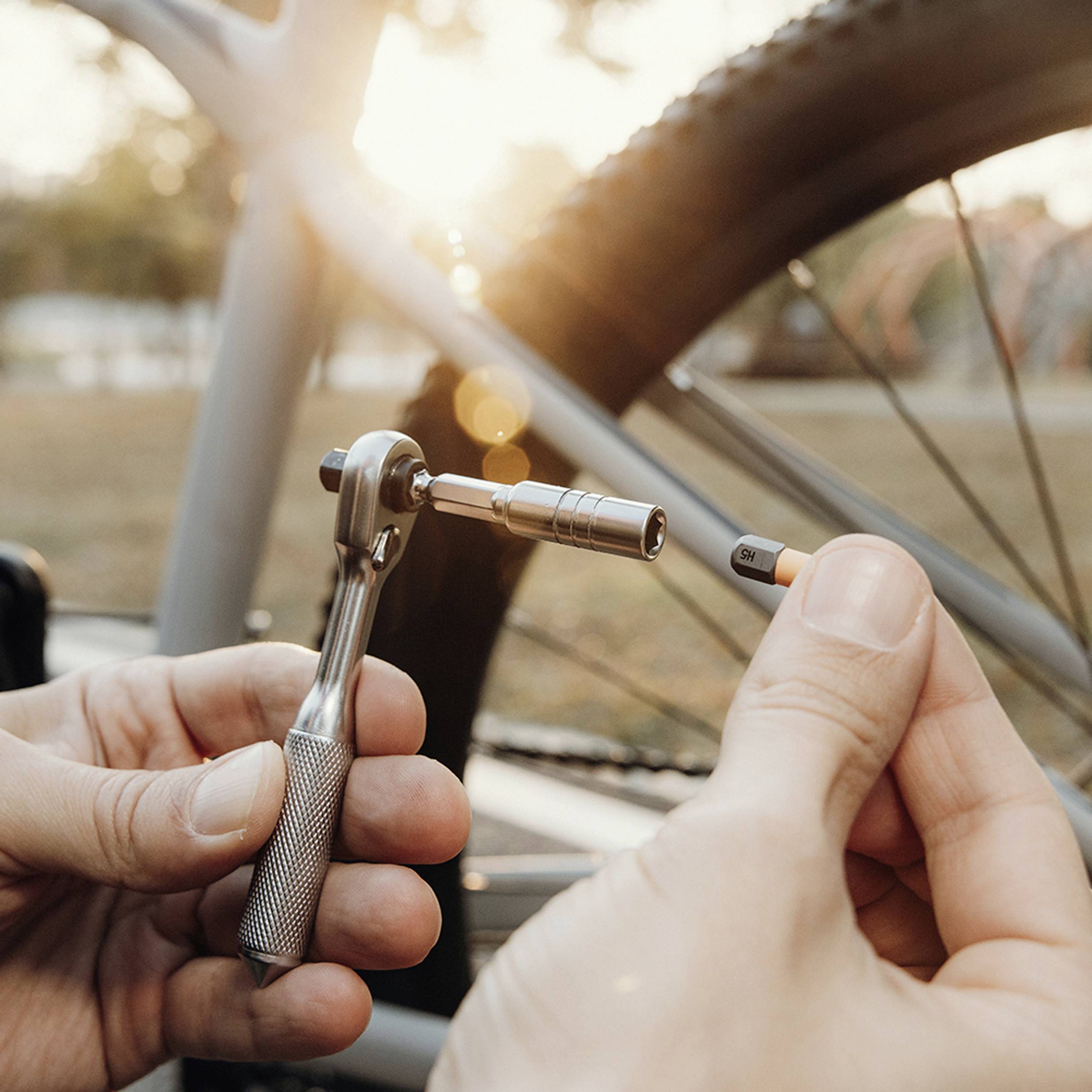 En person använder en skiftnyckel för att dra åt en bult på ett cykelhjul utomhus under solnedgången, vilket belyser vikten av cykelvård.