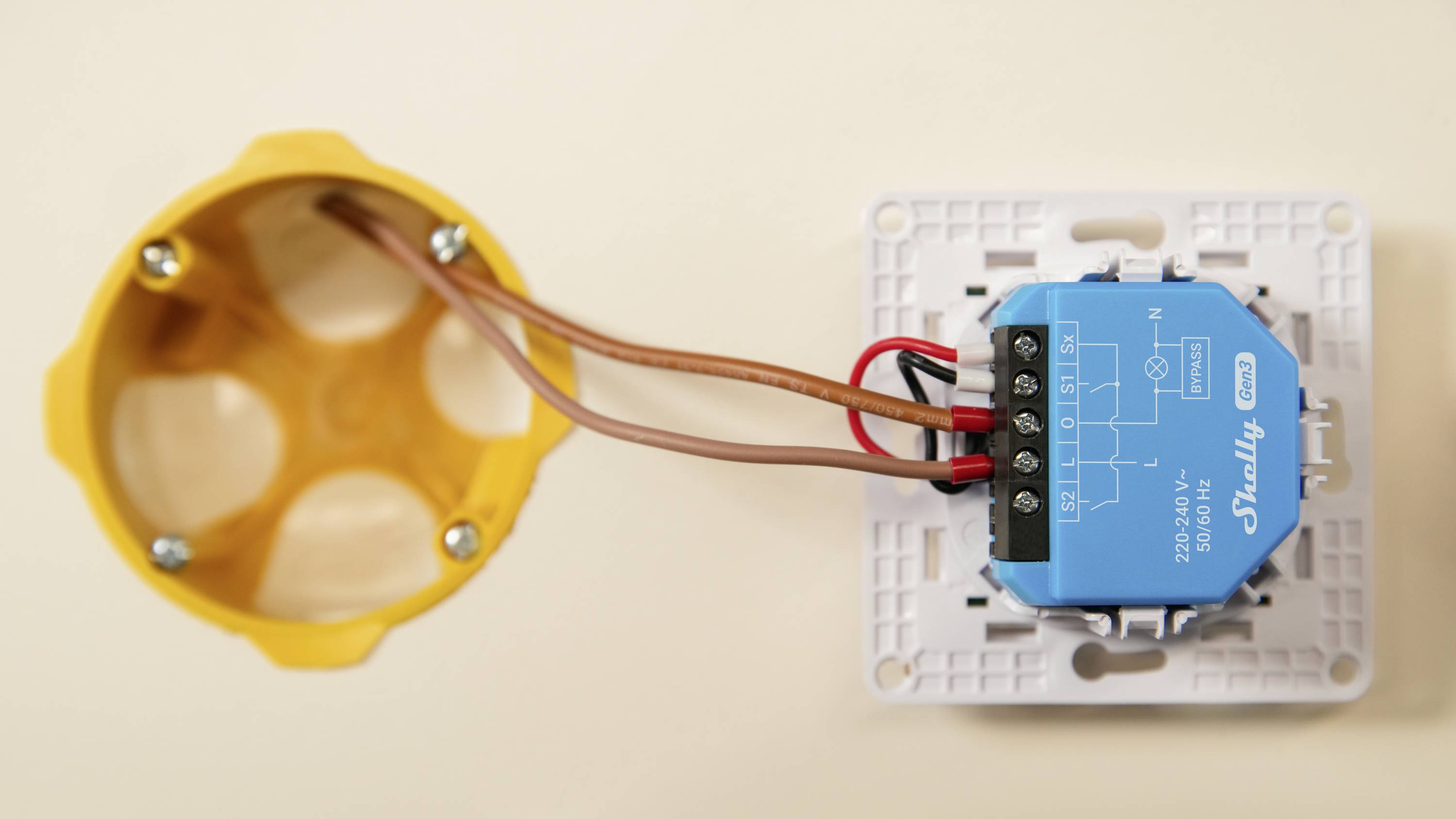 En elektrisk reläenhet med kablar för anslutning, monterad intill en cirkulär väggdosa.