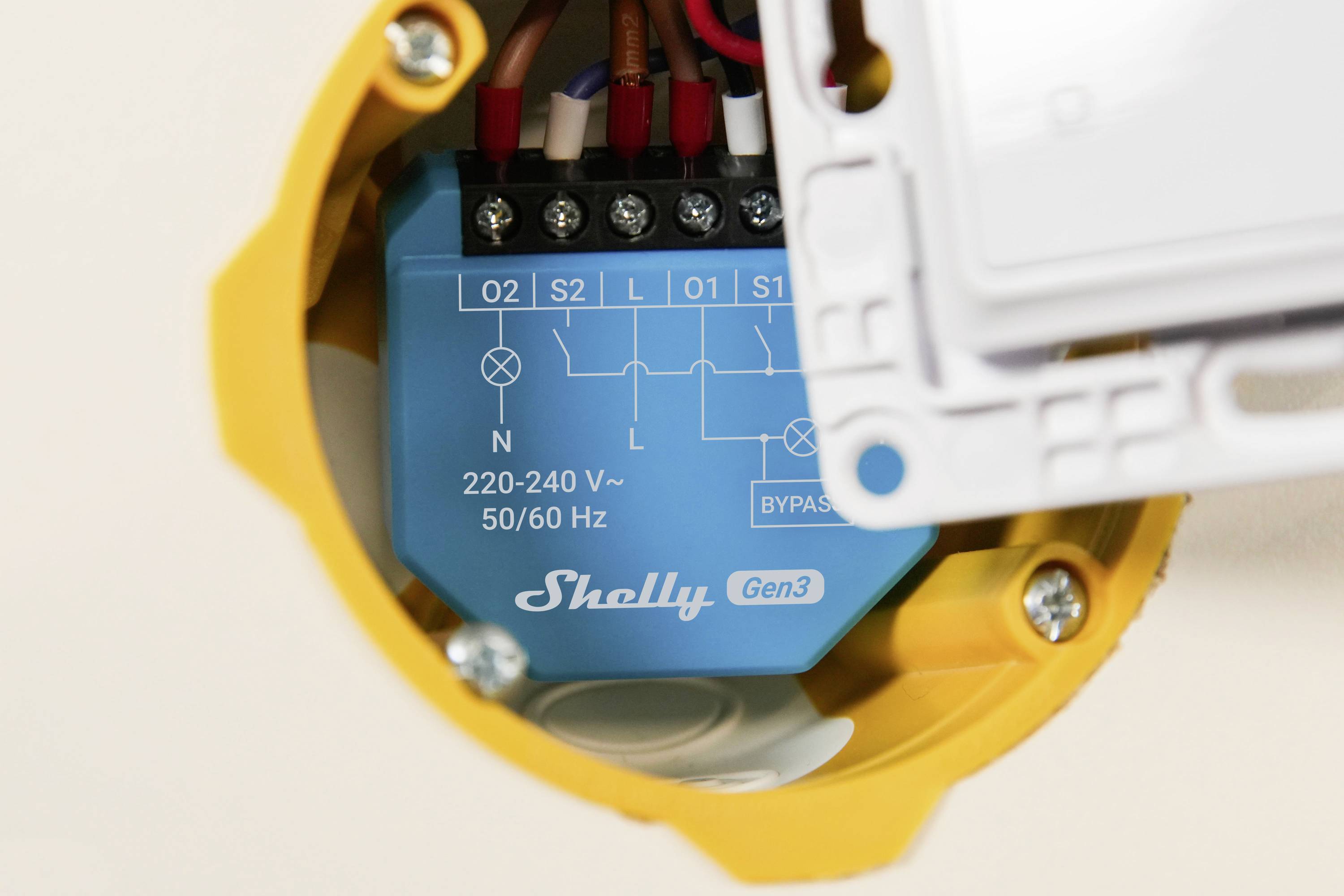 En blå elektrisk relämodul märkt 'Shelly Gen3' innesluten i ett gult hölje. Den visar kopplingsplintar och en 220-240V specifikation.