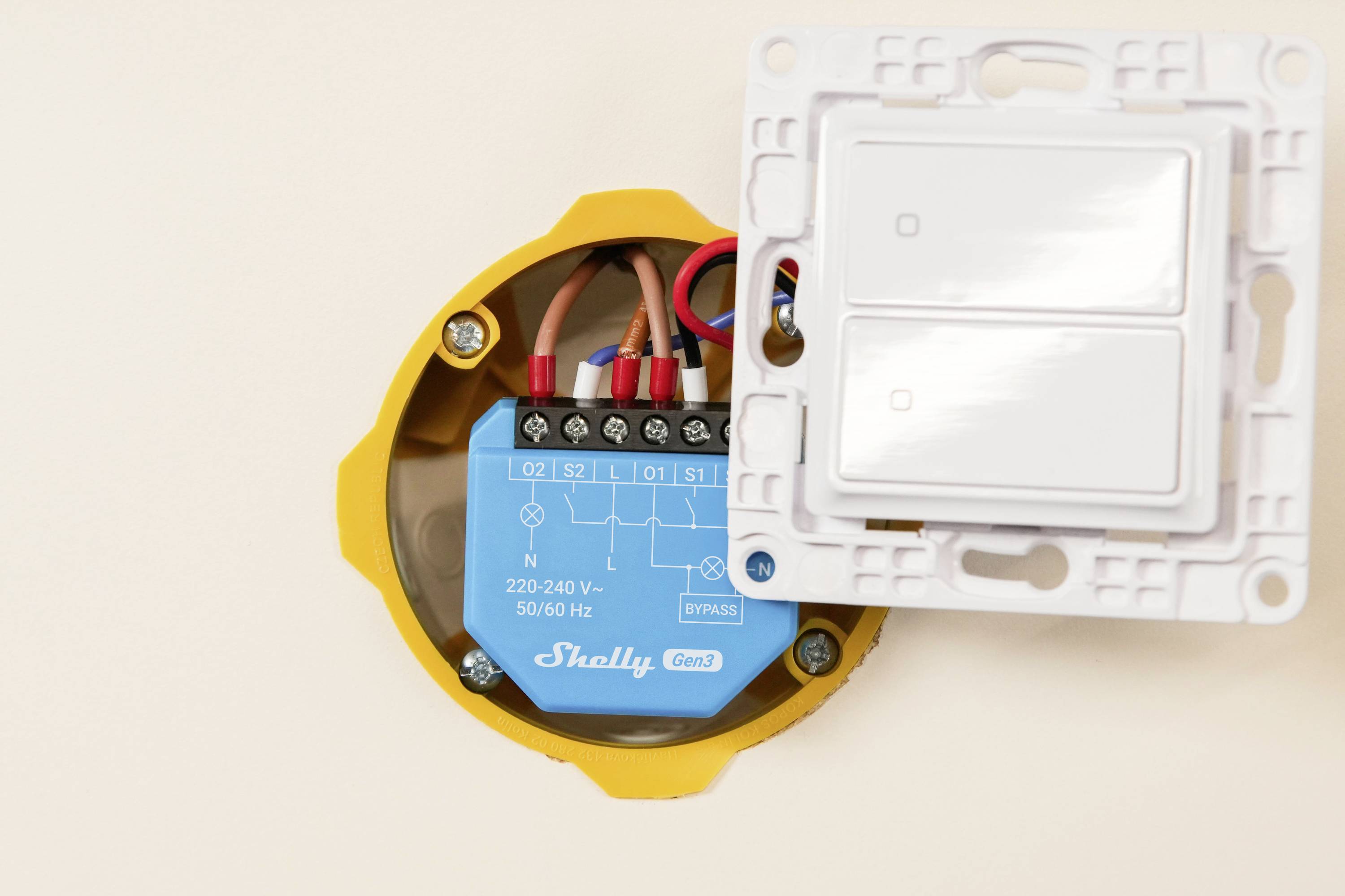 En elektrisk väggströmbrytare är delvis öppen, vilket avslöjar anslutande ledningar och en enhet märkt 'Shelly' med tekniska specifikationer inuti.