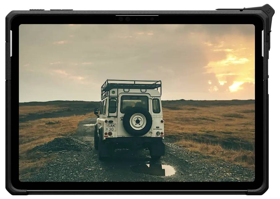 En vit terrängbil kör längs en ojämn grusväg under solnedgången, med ett vidsträckt landskap av fält och en molnig himmel i bakgrunden.