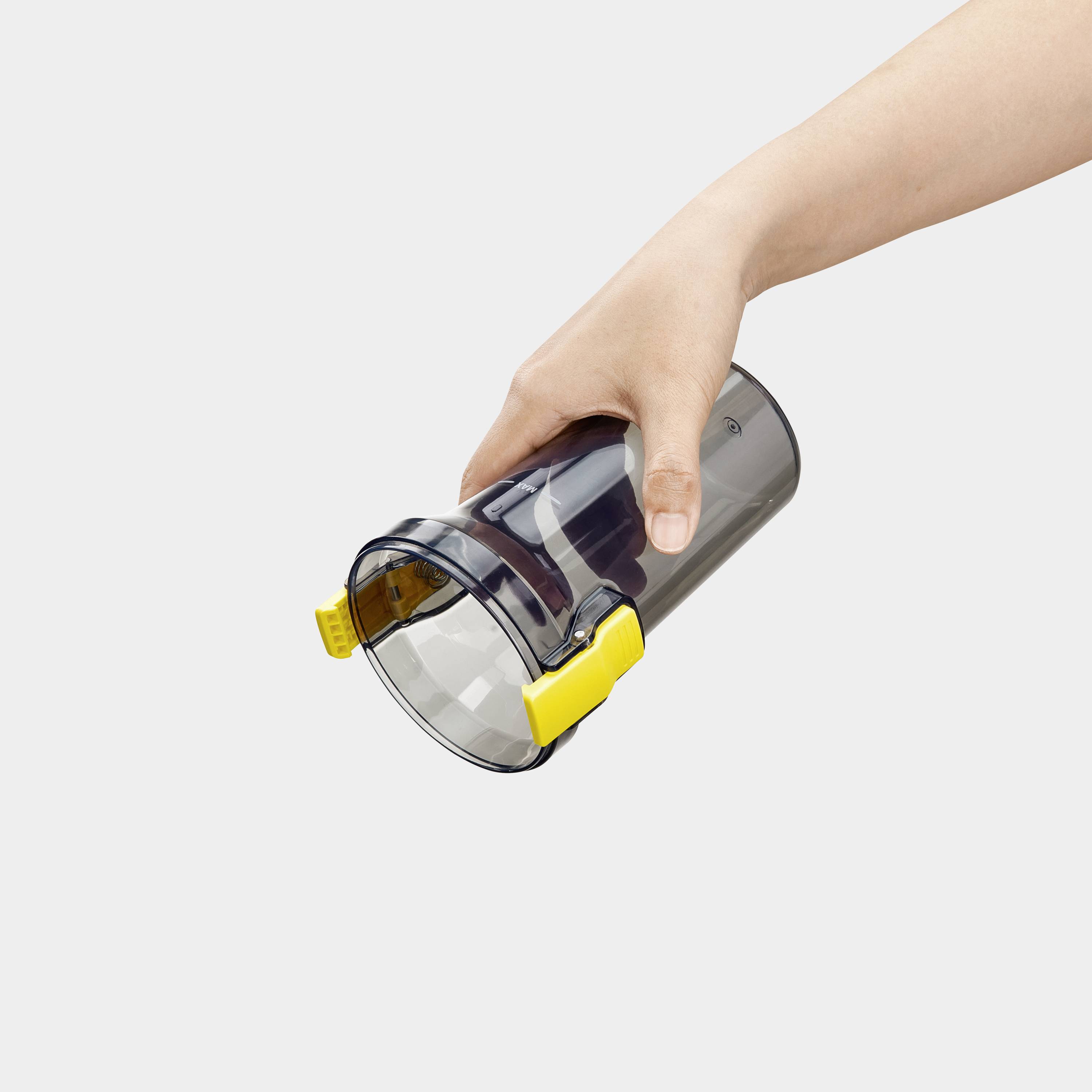 En hand som håller en svart dammcontainer med ett gult handtag, något lutad, vilket visar dess bärbara design och greppfunktion.