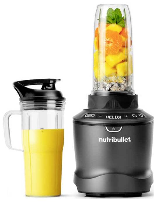 En mixer innehållande frukter och nötter står bredvid en fylld resmugg. Mixerns digitala skärm visar 'HEJ!'.