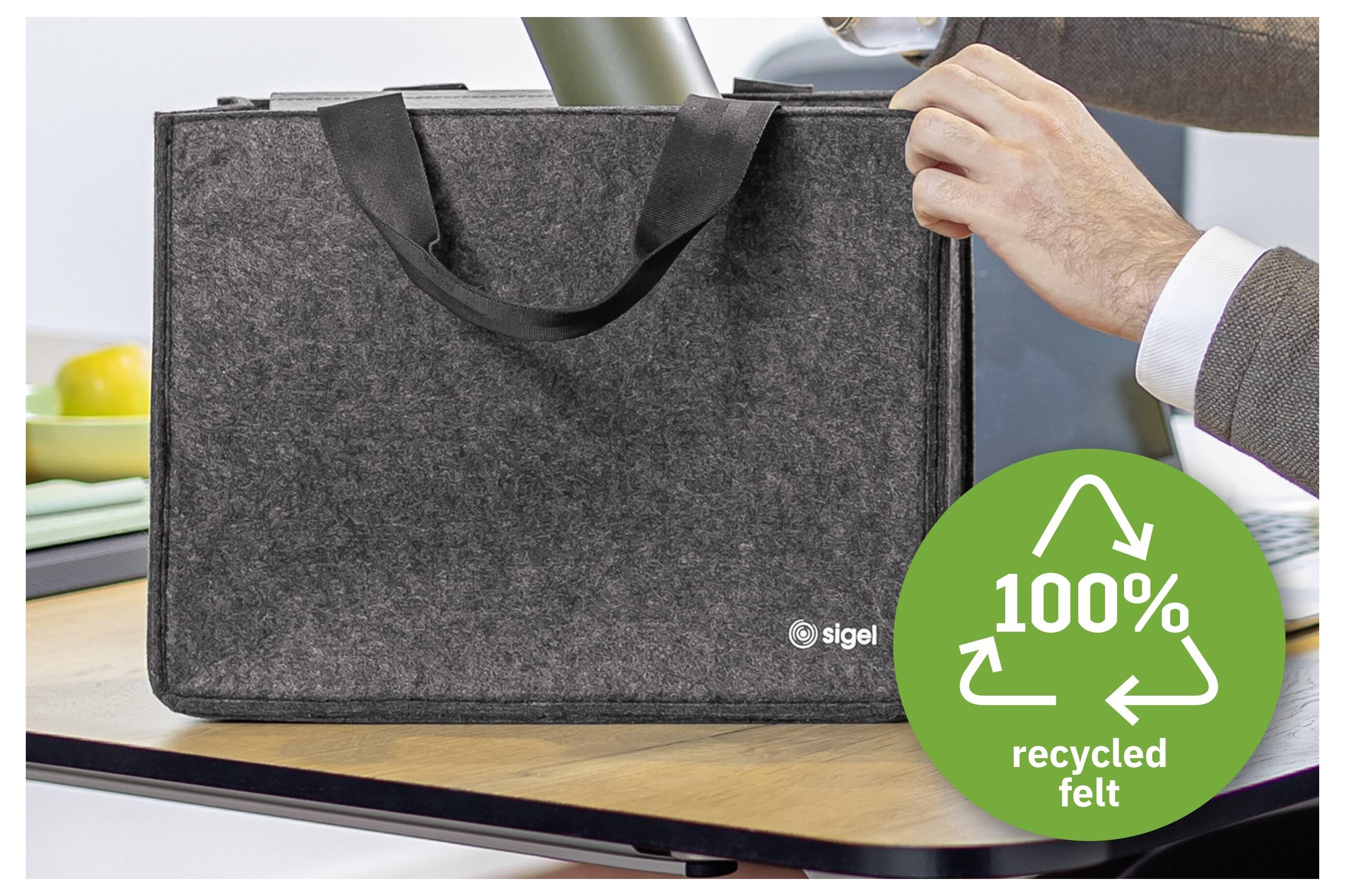 Grå filtad laptopväska med handtag som hålls av en person, märkt med "100% återvunnet filtmaterial" i en grön återvinningsbricka.