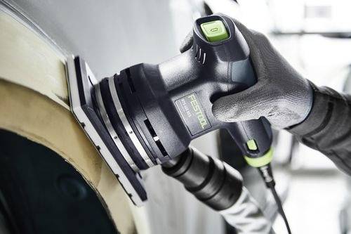 En person använder en Festool-slipmaskin för att jämna till ytan på ett trästycke, bär handskar för skydd och hanterar en sugslang.
