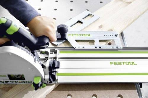En person använder ett Festool-verktyg på ett träplank, placerat på en arbetsställning. Verktyget verkar vara en sågstyrning som assisterar vid precisionskapning.
