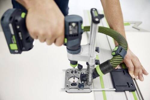 En person använder ett handhållet elverk med en slangkoppling för att skära eller forma ett material på en arbetsbänk.