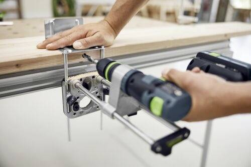 En person använder en borrmaskin för att fästa en metallhållare på en träbalk, vilket visar ett steg i möbelmontage eller reparation.