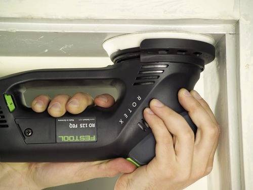 En person använder en Festool ROTEX slipmaskin på en träig hörkkant och visar varsam hantering av elverktyget för precisionslipning.