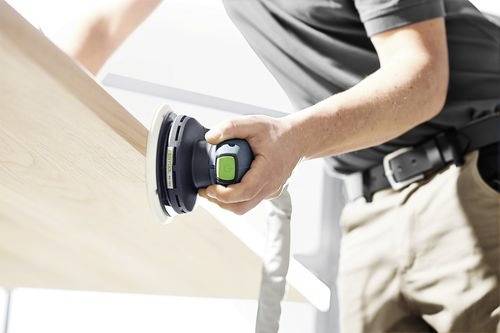 En person slipar en träyta med en elektrisk slipmaskin, med fokus på en slät finish, i en ljus inomhusmiljö.