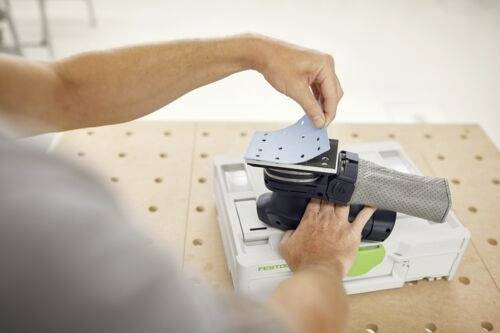 En person placerar ett slipark på en slipmaskin för hand, som är placerad på en arbetsbank.