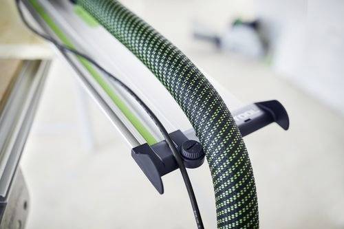 En närbild av en svart och grön strukturerad slang som är fäst vid en metallstyrskena, sannolikt en del av en verkstads- eller verktygsutrustningsuppställning.