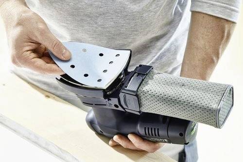 En person som byter slippapper på en elektrisk handslipmaskin. Slipmaskinens gråa dammuppsamlingspåse är fäst vid baksidan.