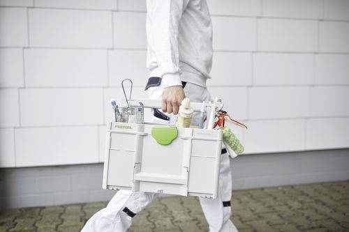 En person i arbetsklädsel som går med en plastverktygslåda fylld med olika målarverktyg, vilket tyder på att de är en professionell målare.
