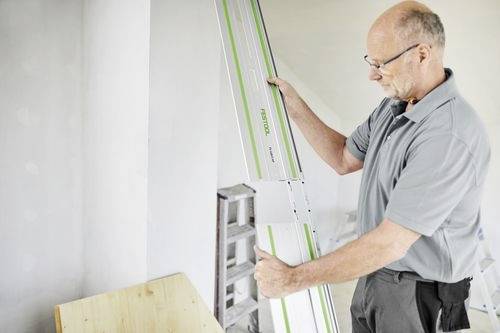 En person som använder en Festool styrskenan för att rikta in material i en verkstadsmiljö, med fokus på träbearbetningsnoggrannhet.