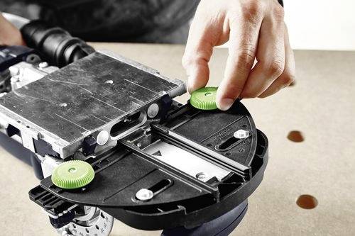 En person justerar en grön knapp på en maskins metalliska och plastiska plattform och visar tekniska justeringar eller underhåll.
