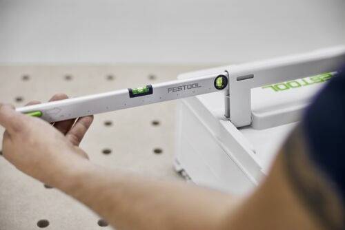 En person justerar ett Festool-verktyg med en vattenpass, vilket säkerställer precision på en perforerad arbetsbänk.