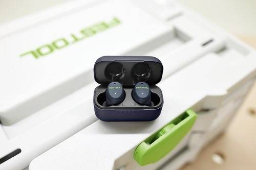 Trådlösa hörlurar med 'FESTOOL'-märkning inuti ett laddningsetui, placerade på en verktygslåda med en grön låsanordning.