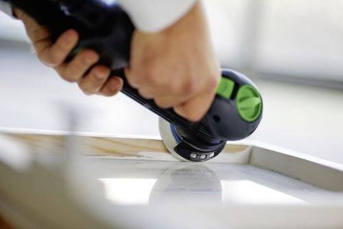 En person använder en handhållen elslip för att jämna till ytan på en träram, med fokus på hörndelen.