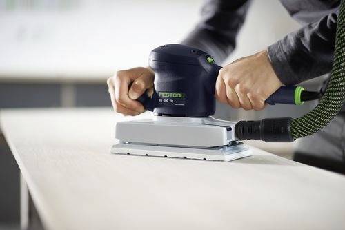 En person som slipar en slät träyta med en elektrisk slipmaskin, med fokus på jämnt tryck och precision.