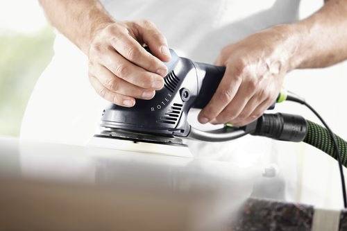Händer manövrerar en elektrisk slipmaskin på en slät yta och visar precision inom träbearbetning eller ytfinishing.
