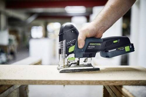 En person som använder en Festool sticksåg för att såga ett trästycke i en verkstad, vilket demonstrerar verktygets precision och kontroll.