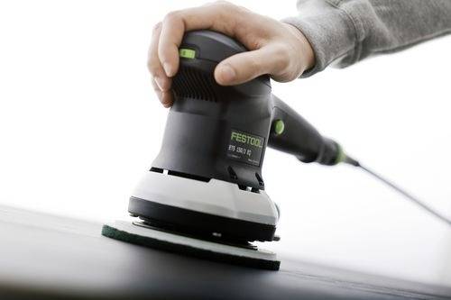 En person som använder ett elektriskt slipverktyg på en plan yta, med fokus på handtaget och slipskivan på verktyget.