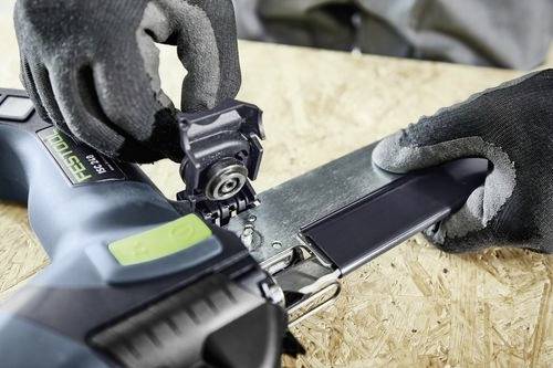 En person med handskar justerar en del på ett elverktyg, troligen på en träarbetsyta, vilket antyder ett sammanhang av byggnation eller reparation.