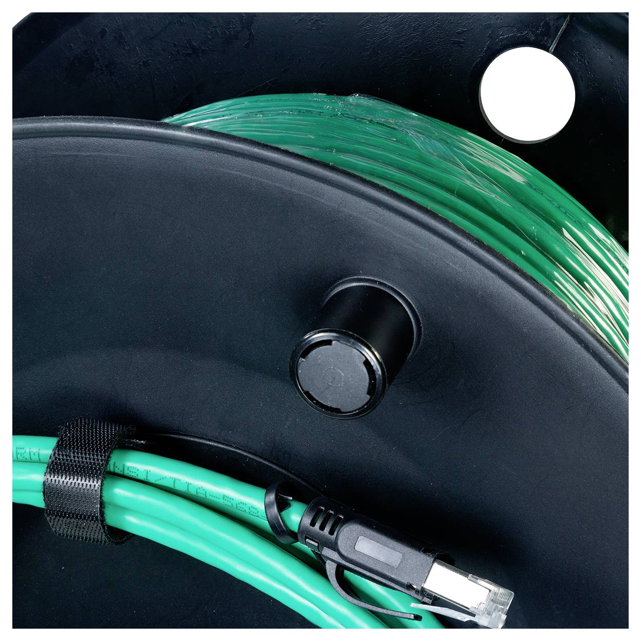 En slingrad grön kabel med en kontakt är lindad runt en svart spole, med en ytterligare del synlig under ett säkrat band.