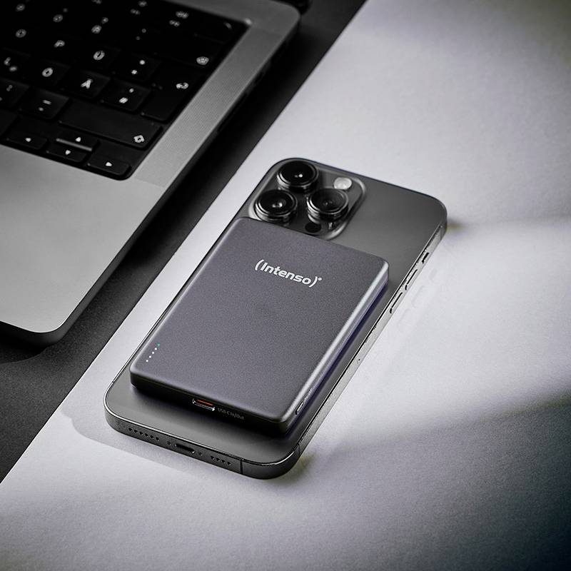 En snygg powerbank med 'Intenso'-märkning vilar bredvid en smartphone intill en bärbar dator, vilket antyder en teknikuppsättning eller laddningsscenario.