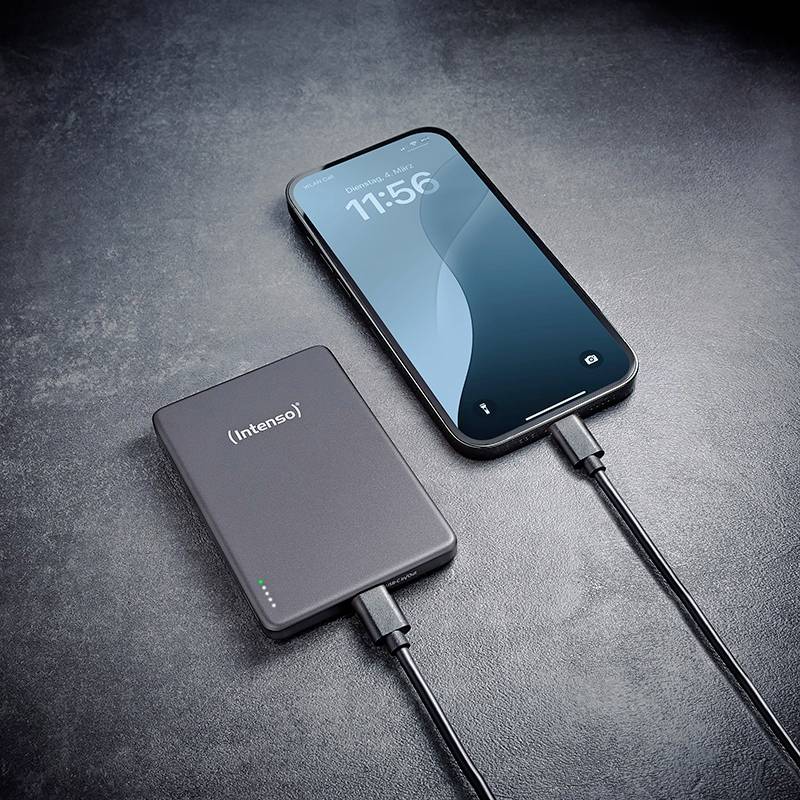 En smartphone som laddas med en Intenso powerbank, båda anslutna via kablar, placerade på en mörk yta. Telefonen visar 11:56.