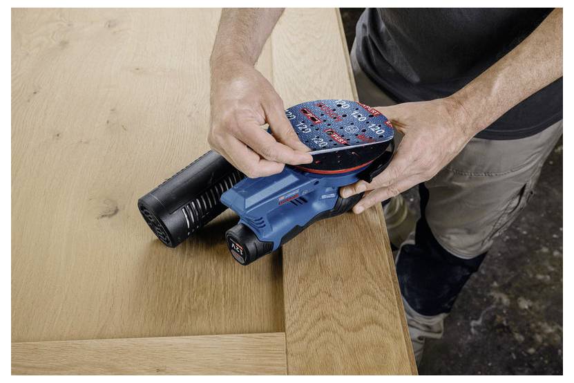 En person slipar kanten på ett träbord med en elektrisk handslipmaskin. Bordet har en ljus finish, och slipmaskinen är blå och svart.
