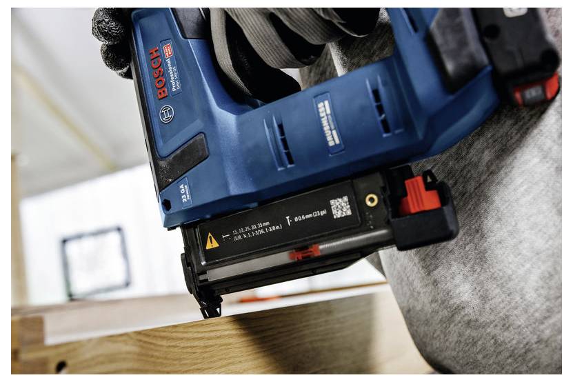 En person använder en blå Bosch spikpistol för att fästa träbitar, med fokus på precision.