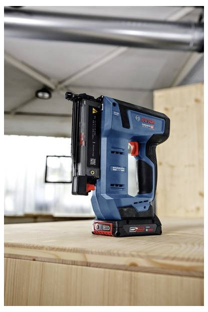 En blå Bosch sladdlös spikpistol står upprätt på en träyta inuti en verkstad och visar upp sin kompakta och ergonomiska design.