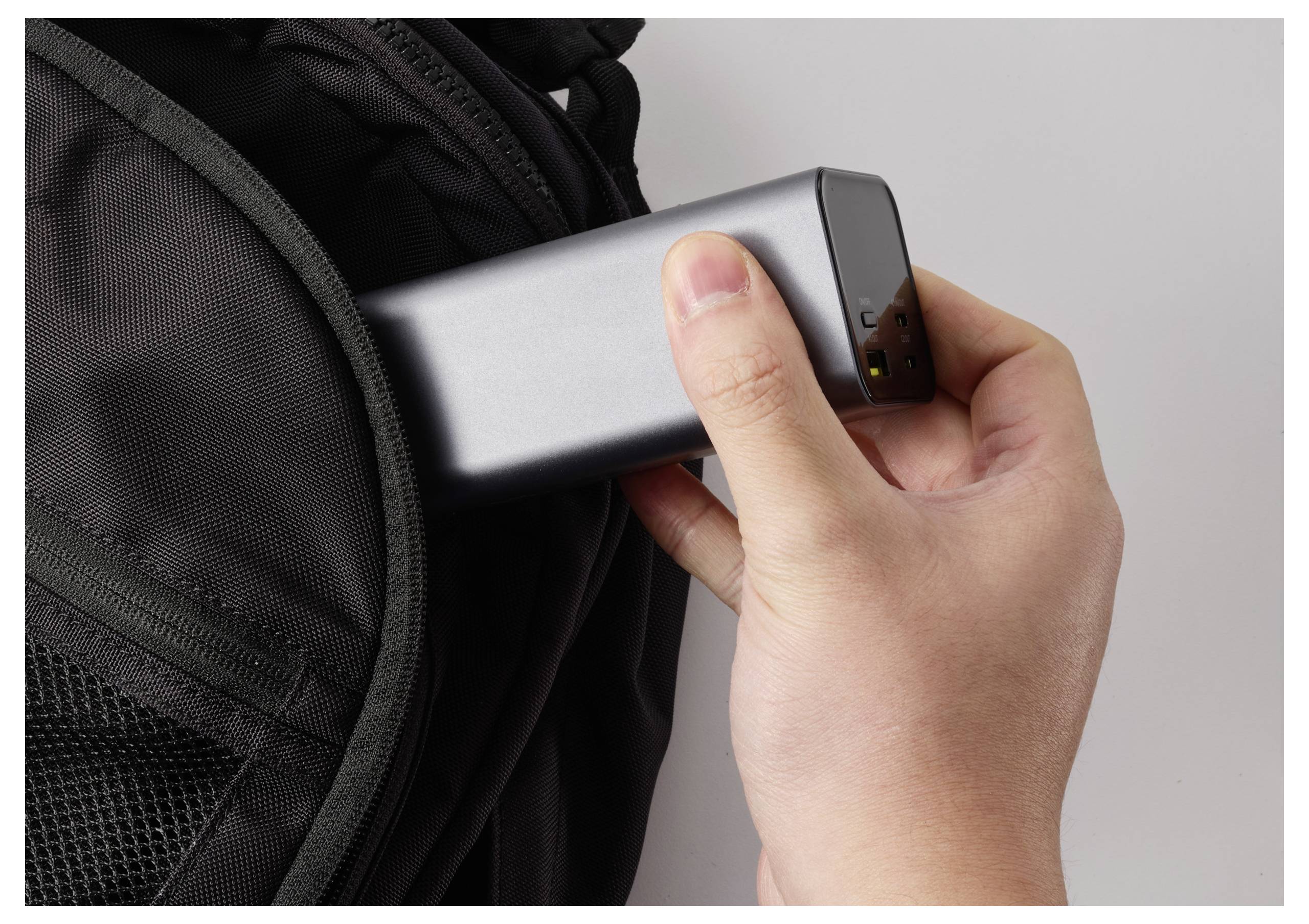 En hand placerar en bärbar powerbank i en ryggsäck, vilket antyder förberedelser för laddning under resan.