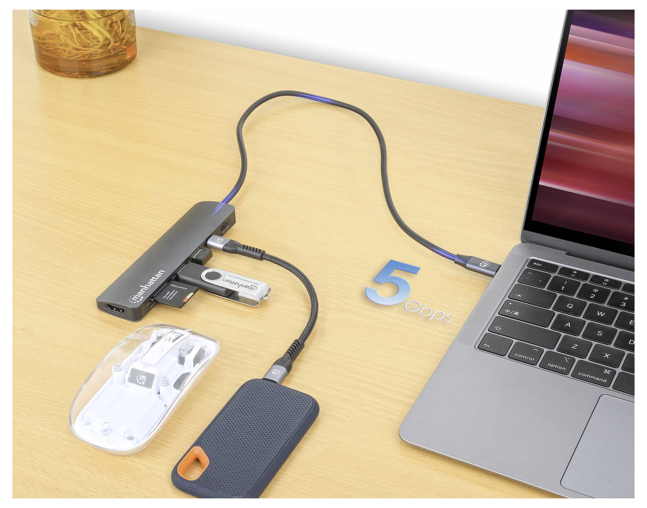 En laptop på ett träskrivbord är ansluten till en multiport-hubb. Hubben har flera anslutna enheter: en mus, ett USB-minne och en extern hårddisk.