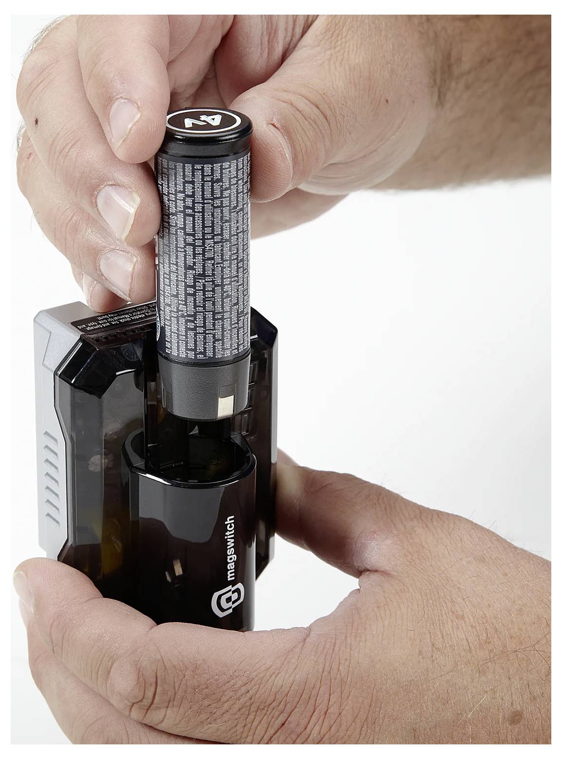 En person för in ett batteri i en svart batteriladdare och håller laddaren stadigt med båda händerna.