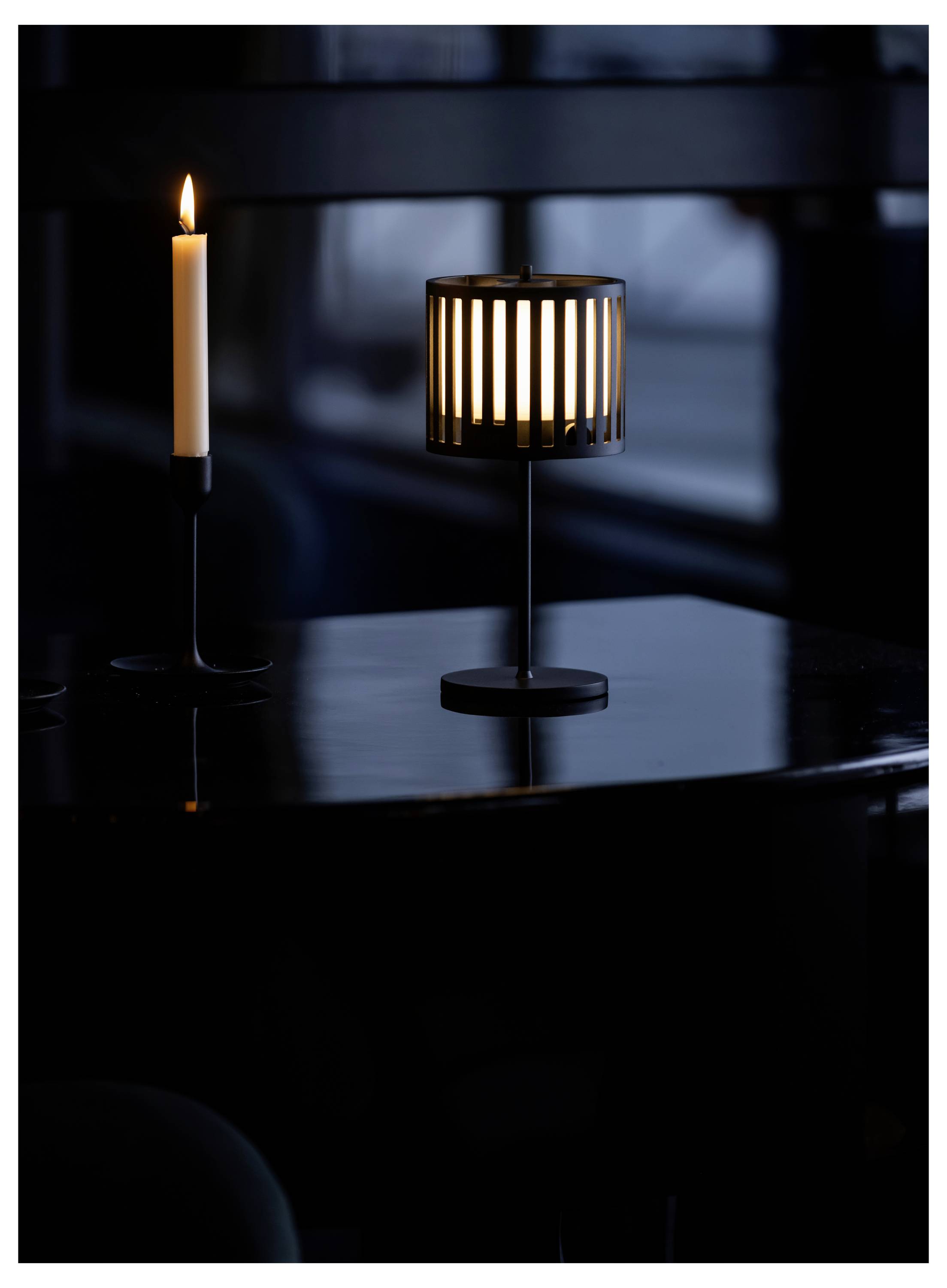 Ett tänt ljus och en lampa med ett vertikalt randig skärm på ett mörkt bord, som ger ett mjukt sken, mot en dämpad bakgrund.