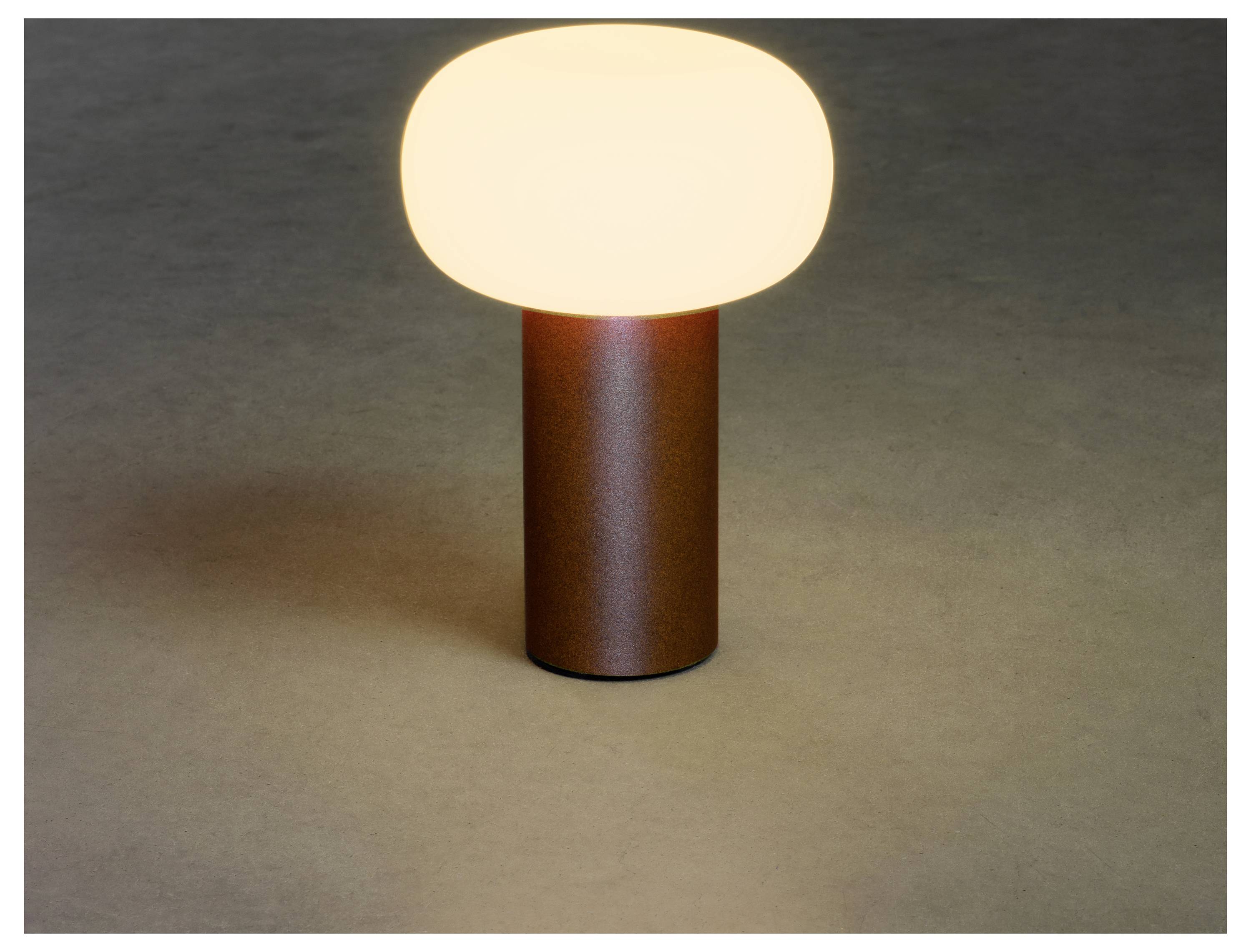 En liten, modern bordslampa med en lysande rundad överdel och cylindrisk bas, som sprider ett varmt ljus, placerad på en neutral yta.