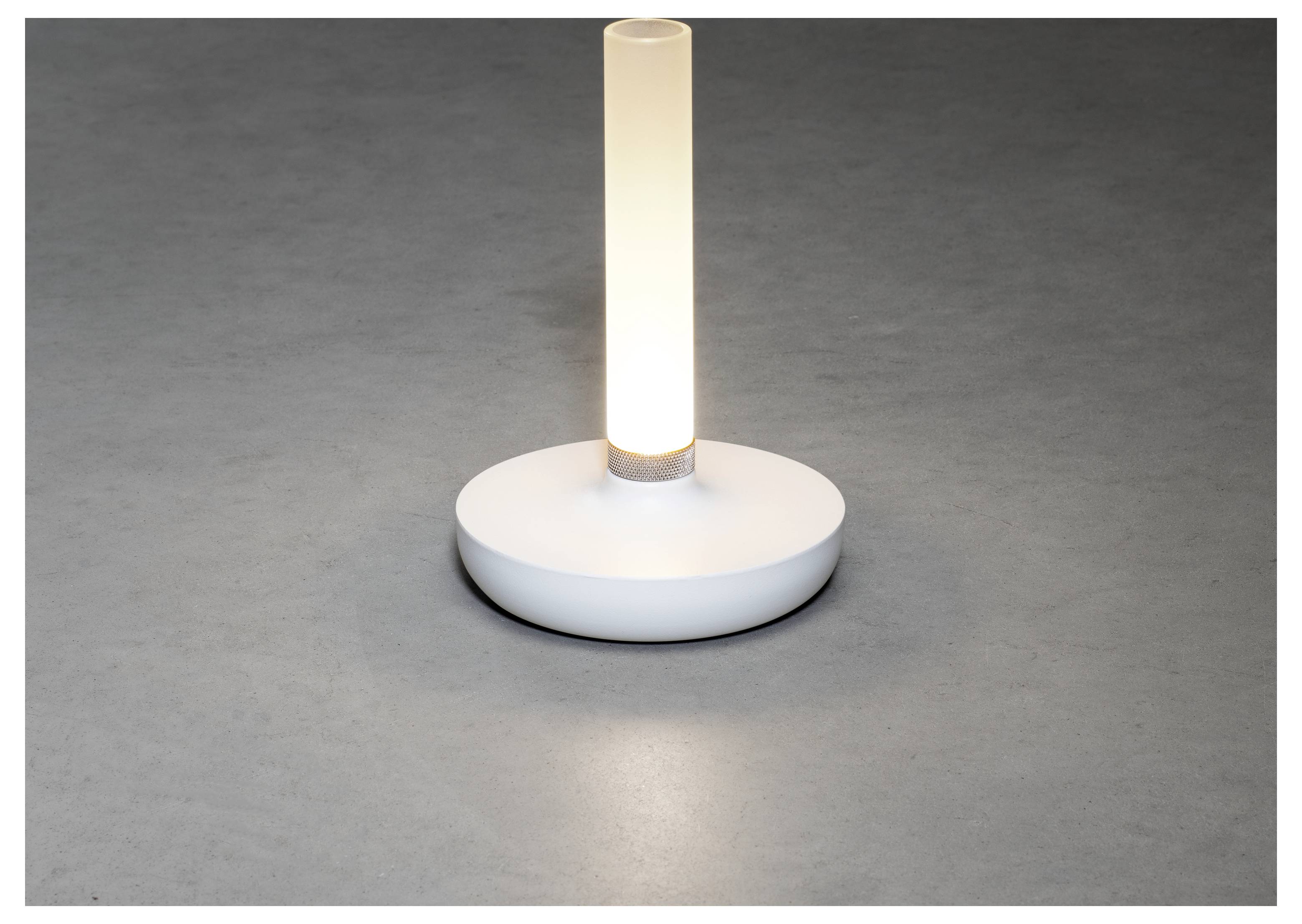 En liten, modern bordslampa med en cylindrisk vit bas och en lysande vertikal ljusrod, placerad på en grå yta.