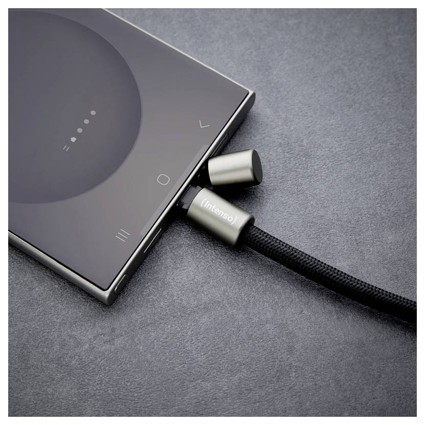 En smartphone laddas via en flätad kabel med metalliska kontakter, liggande på en mörkgrå yta.