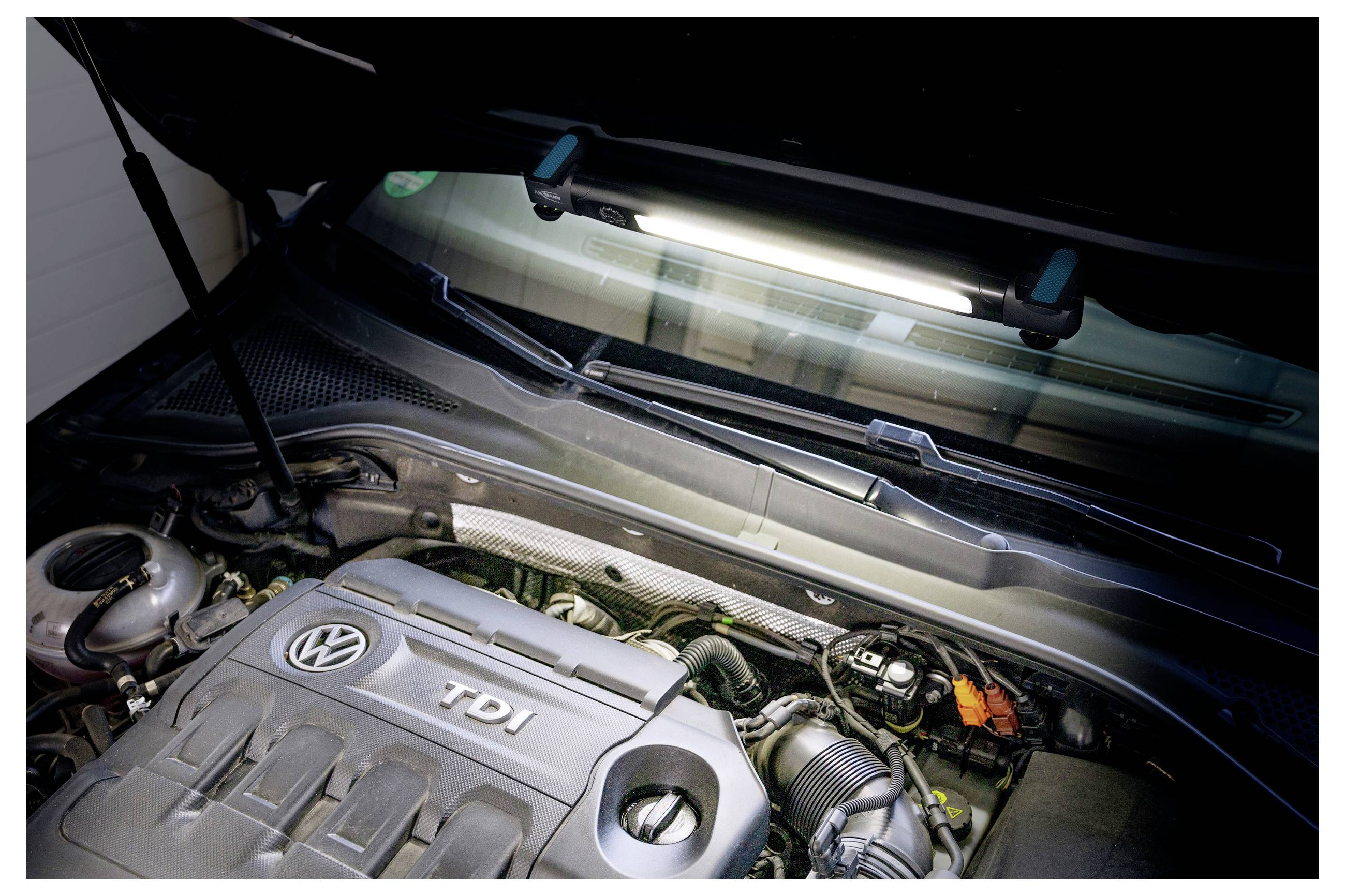 Bilmotorrum som visar en Volkswagen TDI-motor med synliga kablar och komponenter under öppen huv, belyst av ett overheadljus.