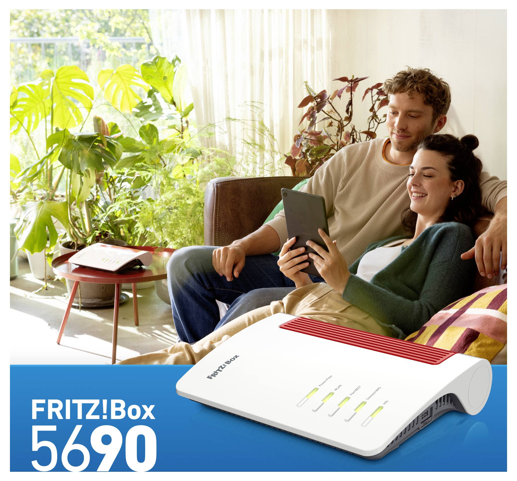Ett leende par sitter på en soffa och tittar på en surfplatta. I förgrunden visas en FRITZ!Box 5690-router med tända LED-indikatorer.