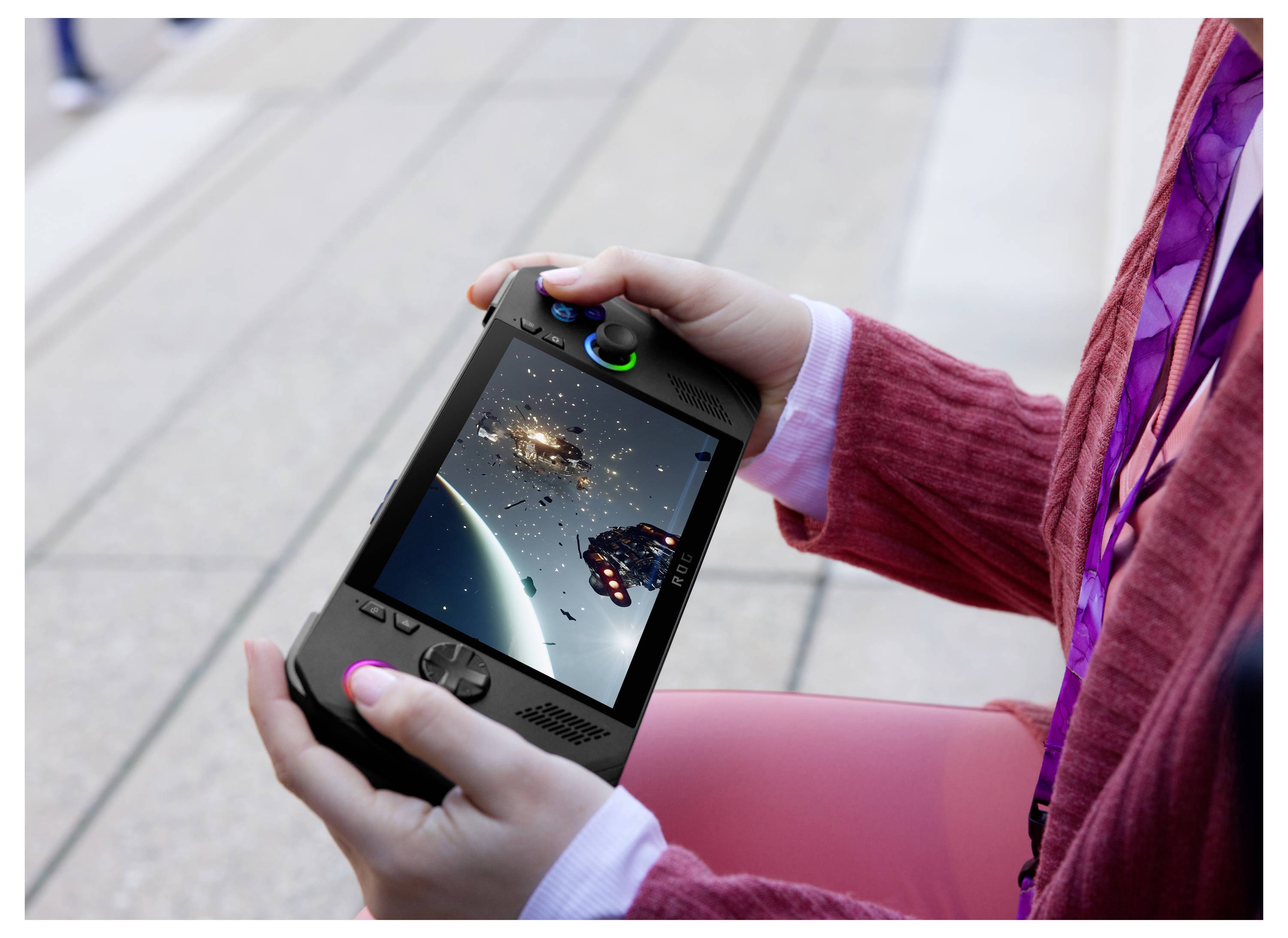 En person som håller i en handhållen spelkonsol där ett rymdtema-spel visas, med rymdskepp och en planet i bakgrunden.