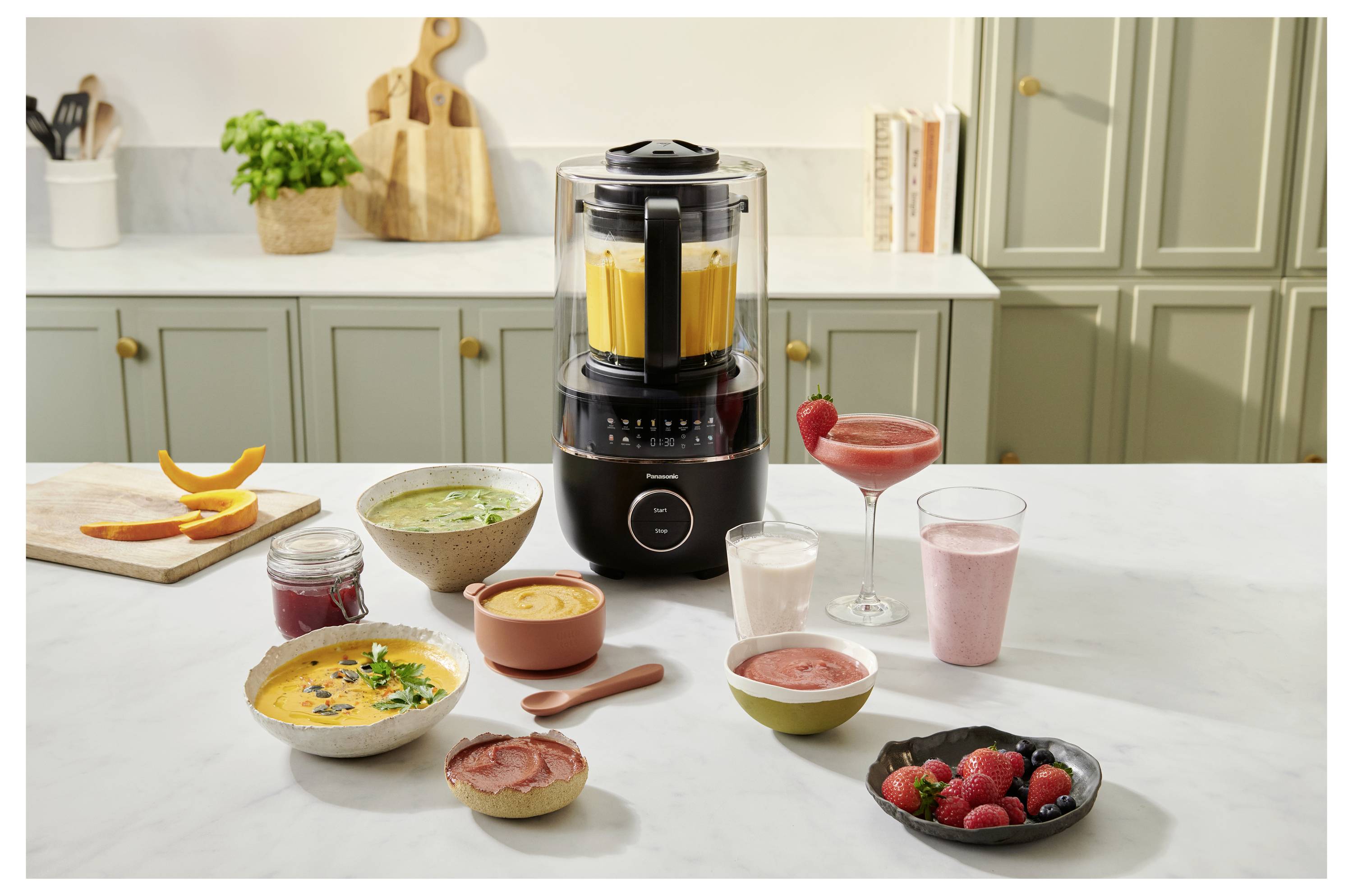 Ett modernt kökssettning med en blender med display, omgiven av färggranna smoothies, soppor och färska fruktskålar.